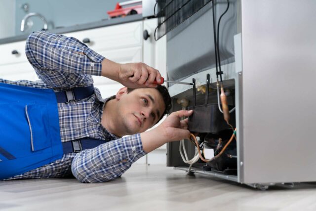 Fridge being repaired in Edmonton, a repairman has a screwdriver out and he is putting the back of the fridge back together after fixing the appliance.