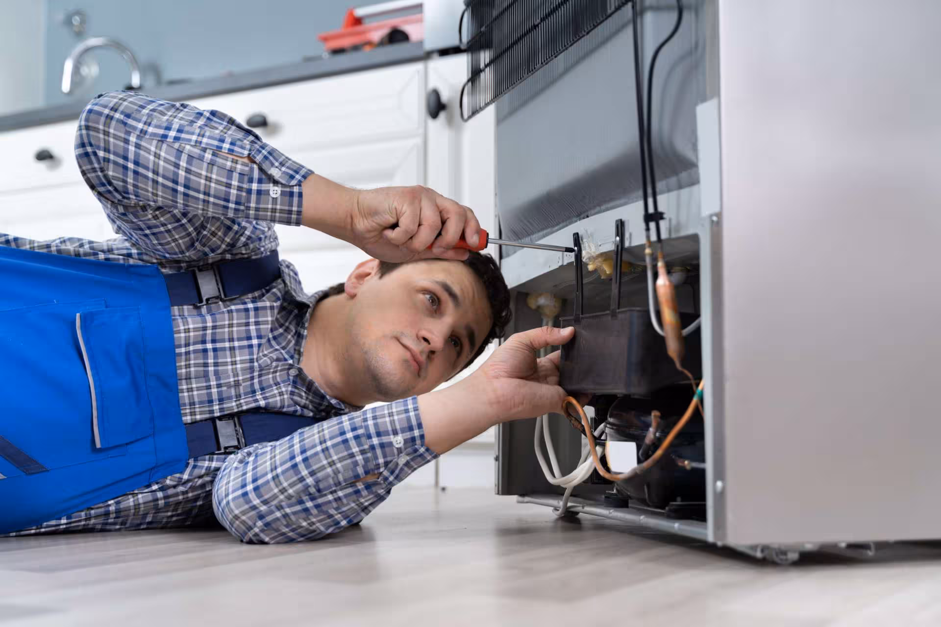 Fridge being repaired in Edmonton, a repairman has a screwdriver out and he is putting the back of the fridge back together after fixing the appliance.