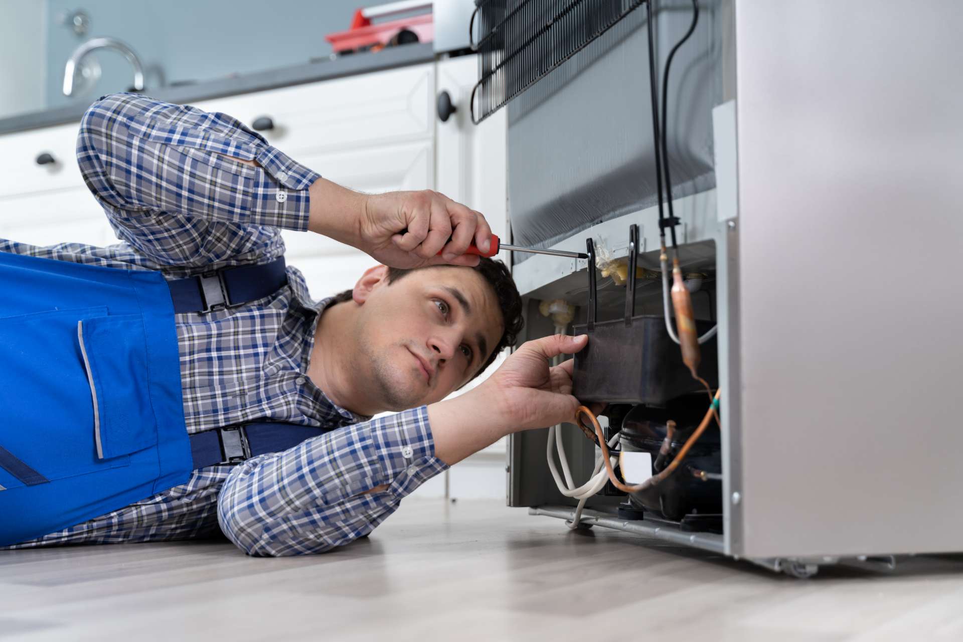 Fridge being repaired in Edmonton, a repairman has a screwdriver out and he is putting the back of the fridge back together after fixing the appliance.