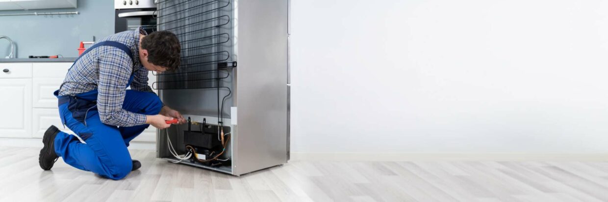 A repairman has a screwdriver out and he is taking the back of the fridge off to investigate the issues and fix the appliance in Edmonton.