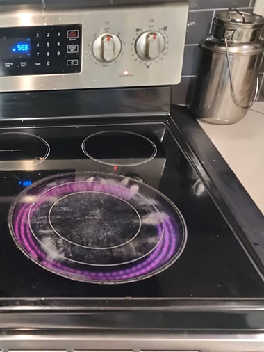 Wide view of a Samsung electric range in a residential kitchen. The bottom-right Fast Boil burner is glowing pink, and the Cooktop On indicator light is lit on the control panel, even though all knobs are in the OFF position.