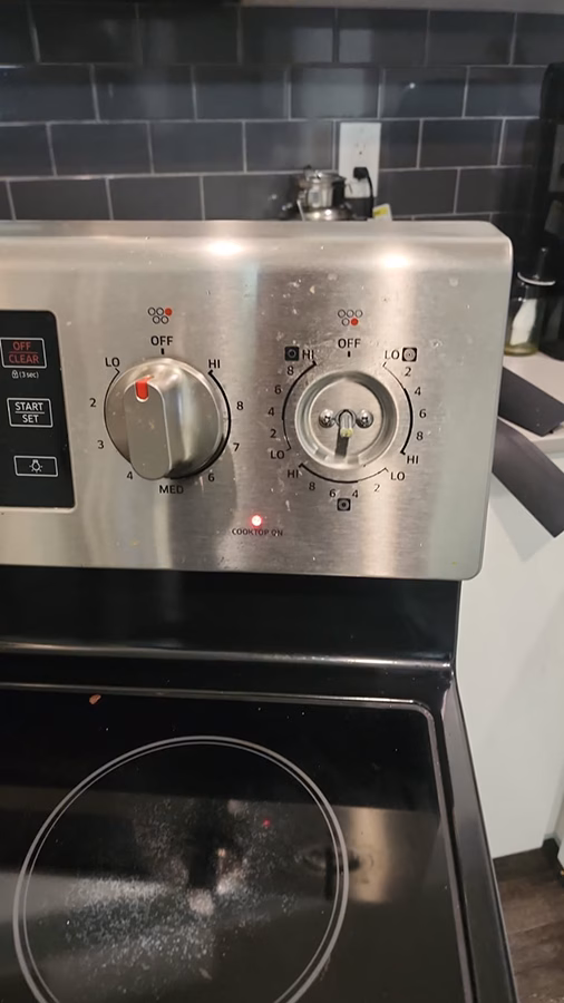 The right burner knob has been removed from the Samsung stove control panel, exposing the bare metal shaft of the infinite switch underneath. The repair process has begun.